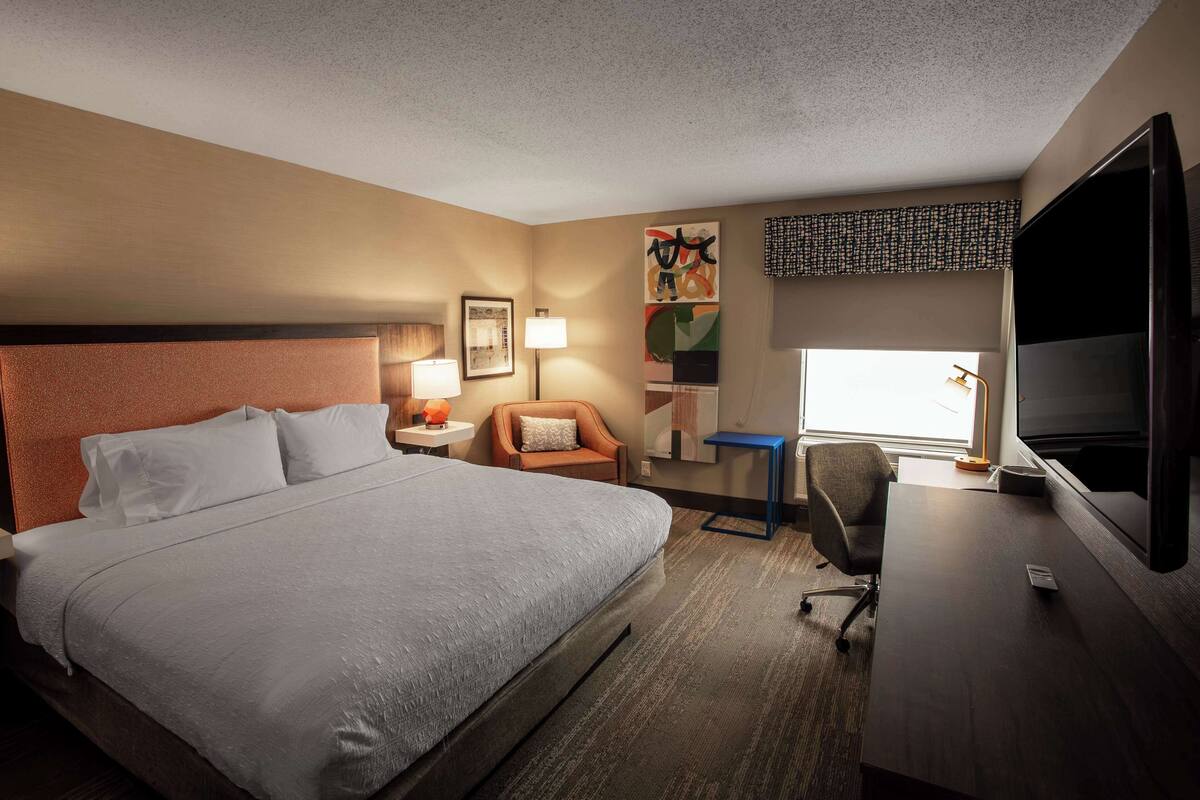 A hotel room with a large bed, a desk, a chair, a TV, and a window with a view.
