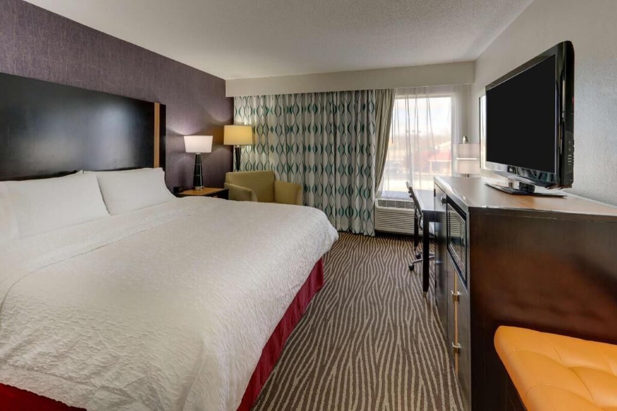 A hotel room with a large bed, a desk with a television, a chair, and a sofa.