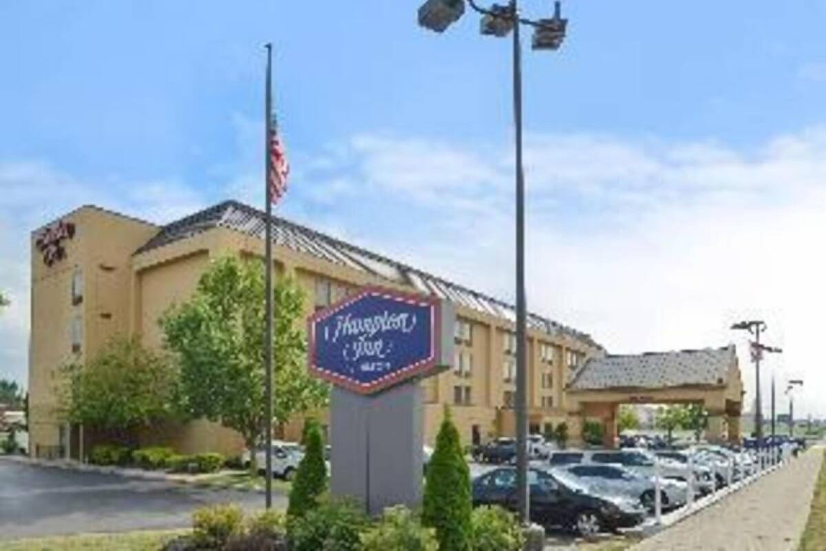A hotel with a sign reading 'Thousand Trails Hotel,' a parking lot with cars, and a clear sky.