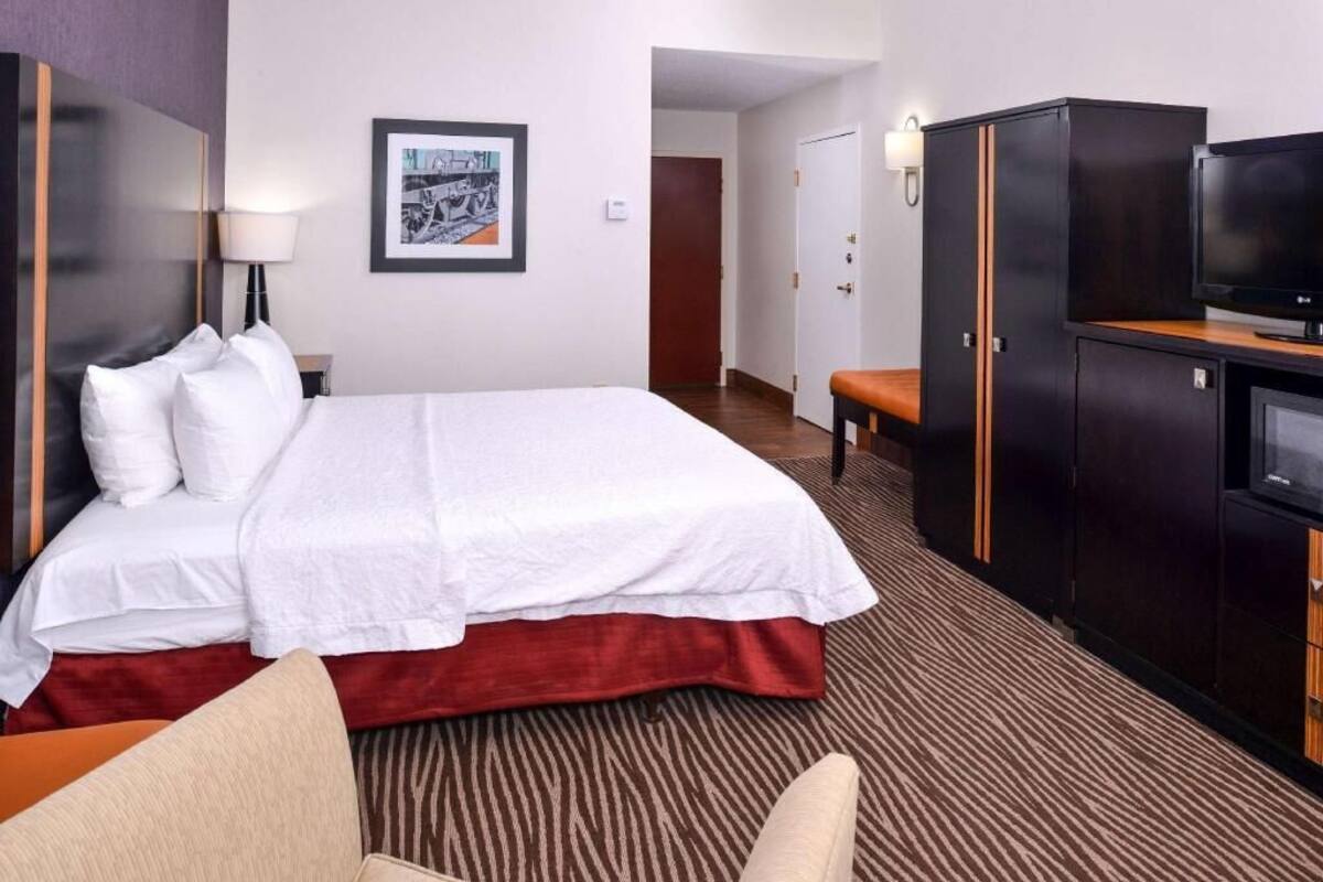 A hotel room with a bed, a desk, a television, a wardrobe, and a framed picture on the wall.