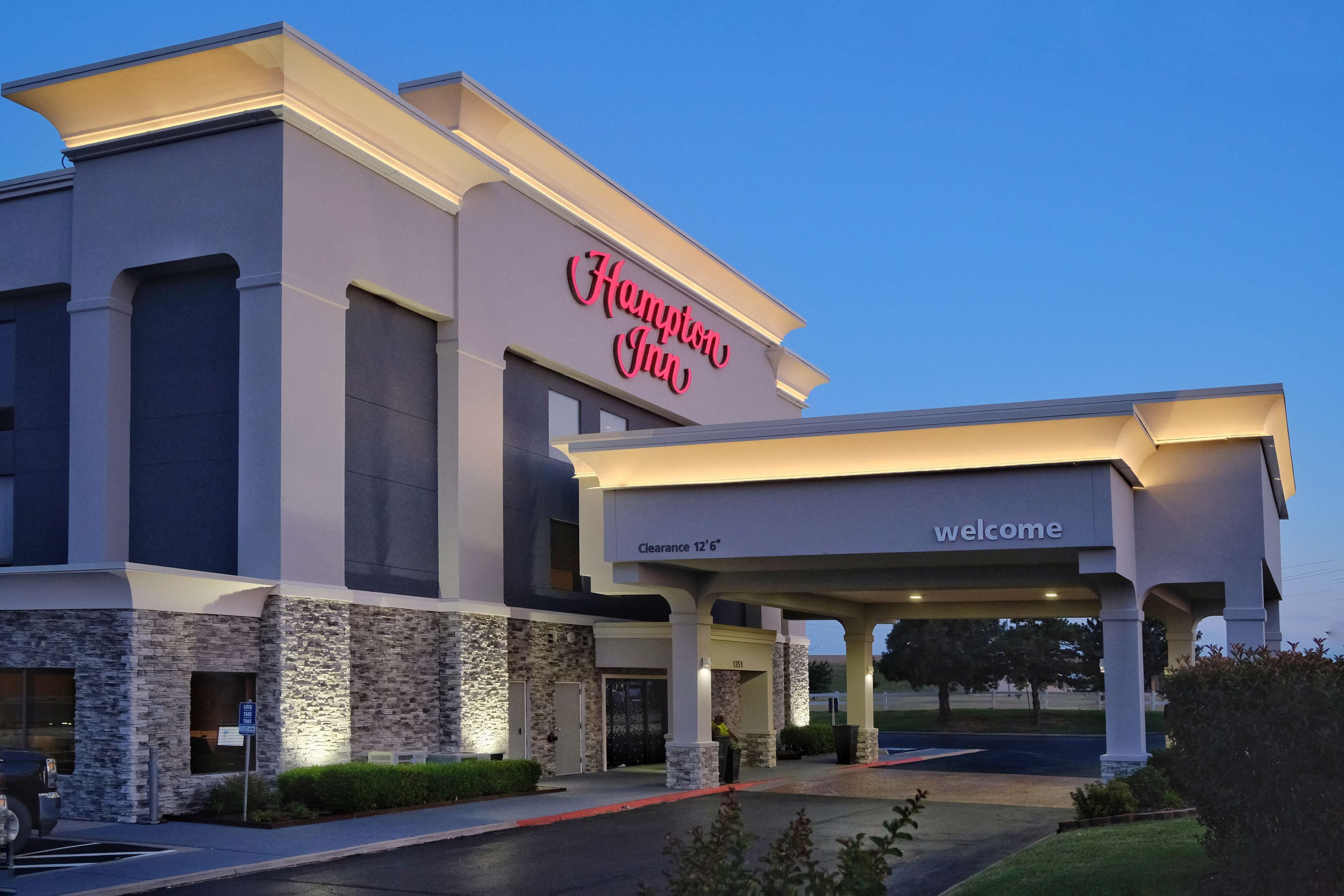 Edificio de Hampton Inn con fachada de piedra, un letrero de 'Bienvenido' y un letrero de 'Altura libre 3.8 metros'.