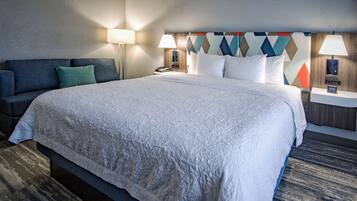 A hotel room with a large bed, a sofa, two bedside tables with lamps, and a geometric-patterned headboard.