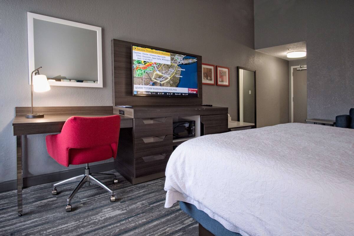 A hotel room with a bed, desk, chair, TV, and a map on the wall.