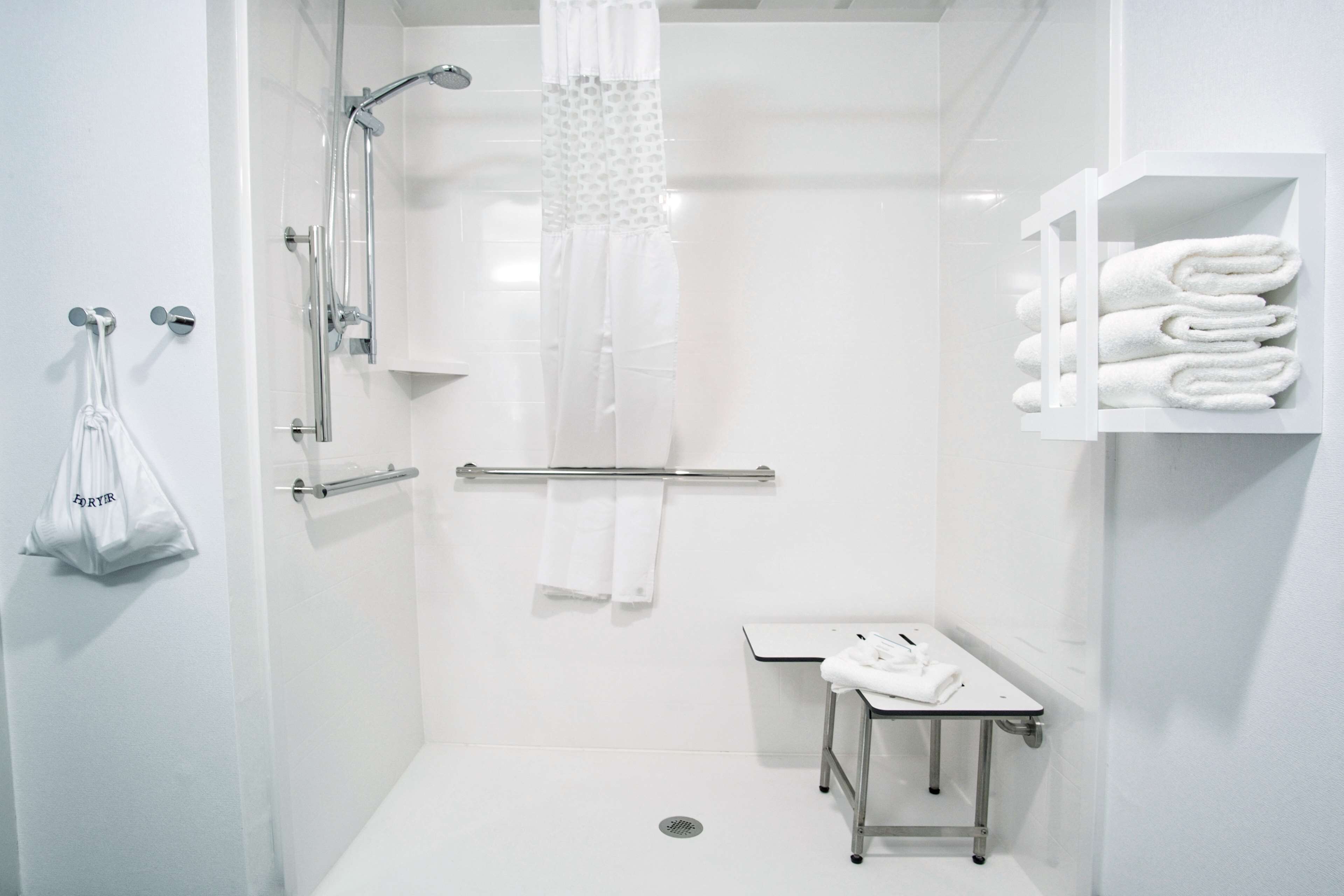 A modern bathroom with a shower, a toilet, and a sink. There are towels and a bag hanging on the wall.