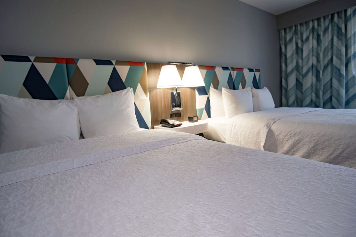 A hotel room with two beds, a nightstand with a lamp, and a patterned headboard.