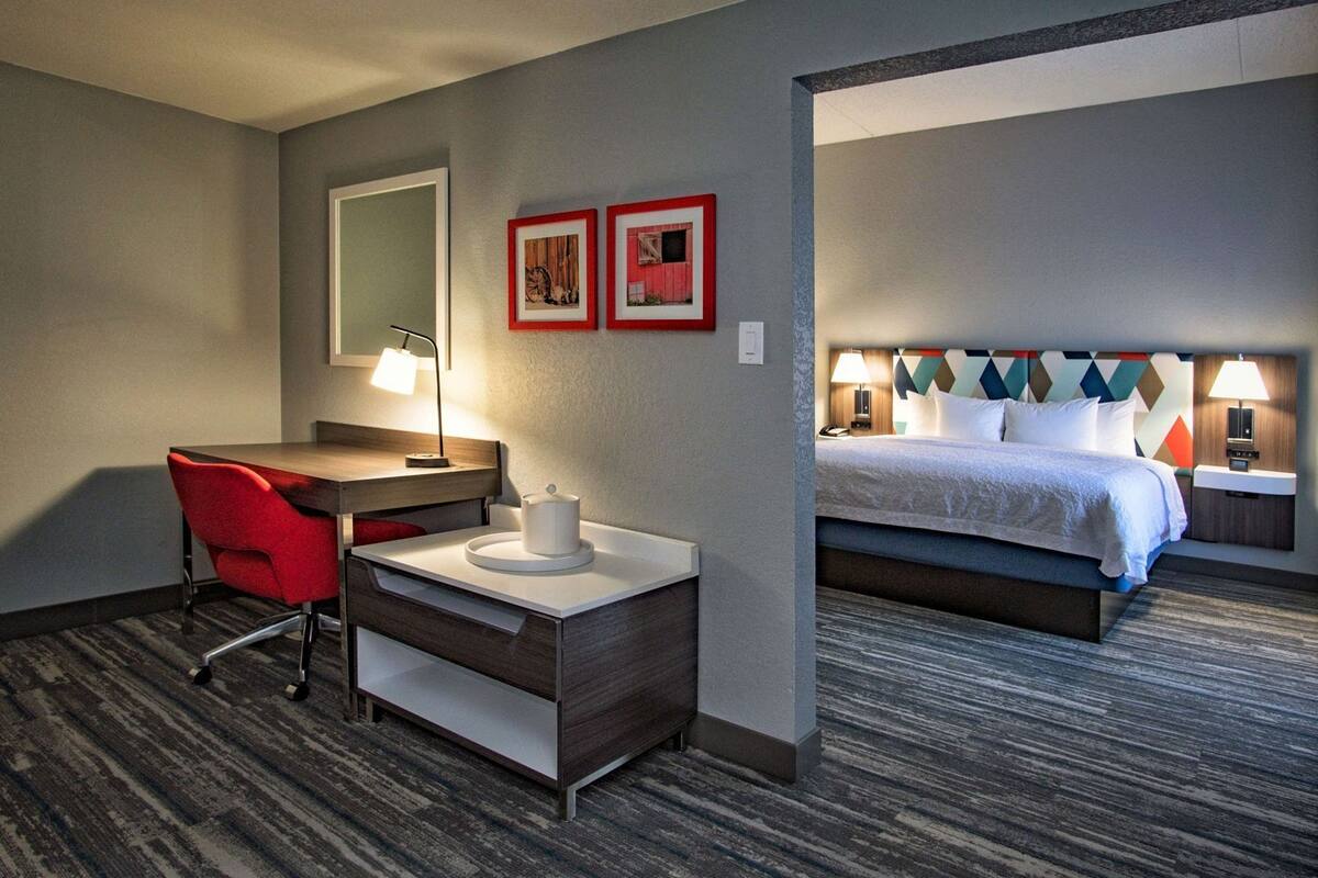 A hotel room with a desk, chair, bed, and nightstand.