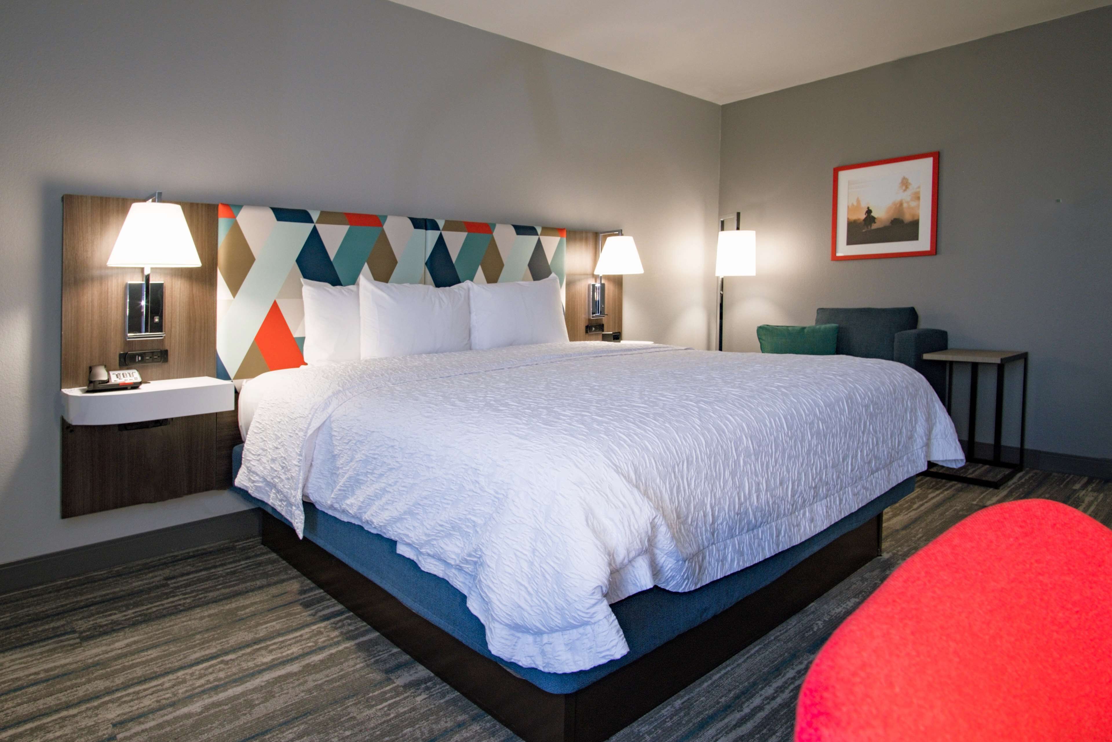 A hotel room with a large bed, two bedside tables with lamps, a small desk, and a chair.