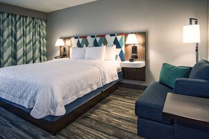 Una habitación de hotel con cama, mesitas de noche, un sofá y una cortina estampada.