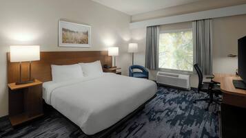 Een hotelkamer met een groot bed, twee bedlampen, een bureau met stoel, een televisie en een raam met gordijnen.