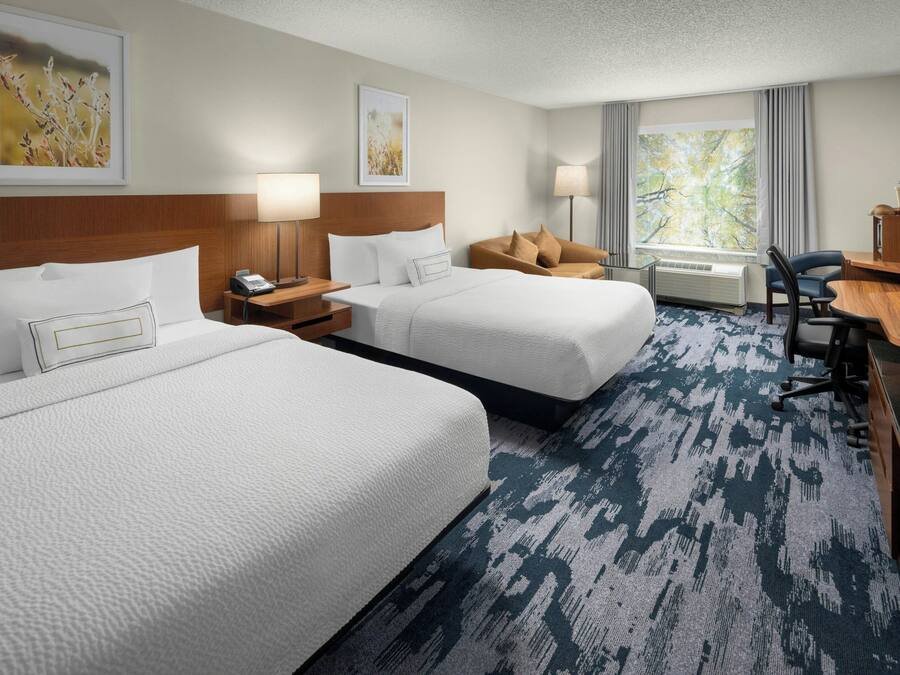 A hotel room with two beds, a desk, a chair, a TV, and a window with curtains.