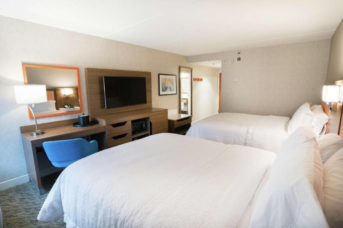 A hotel room with two beds, a desk with a chair, a television, and a mirror.