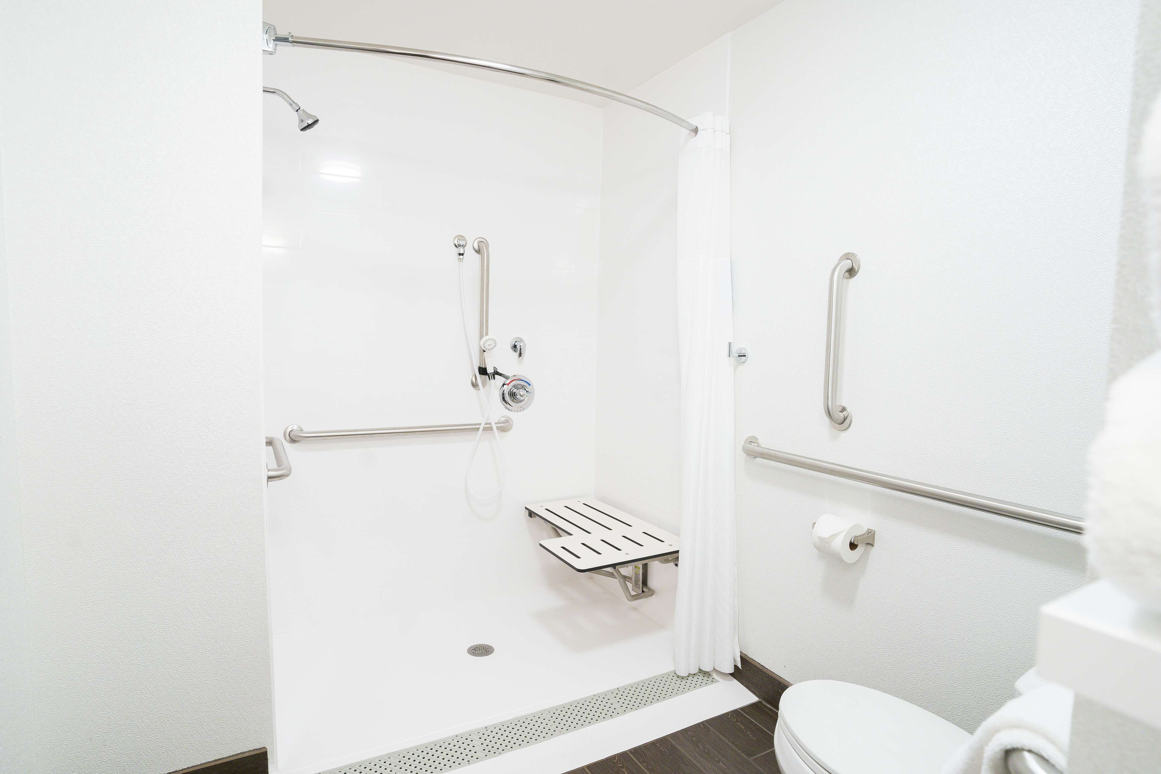 Een moderne badkamer met douche, toilet en handgrepen.