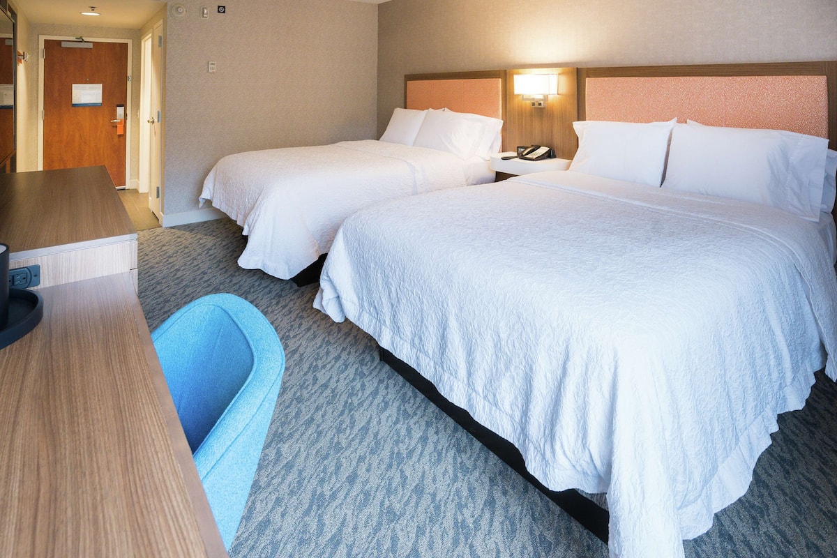 A hotel room with two beds, a desk, and a chair.