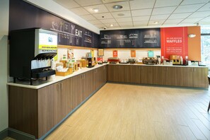 A modern kitchen area with a waffle station, coffee machines, and a counter with various food items.