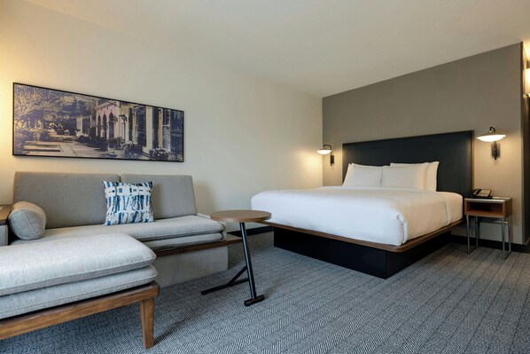 A hotel room with a bed, a sofa, a small table, and a wall-mounted artwork.