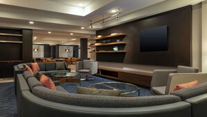 Un salon moderne avec un canapé d’angle aux lignes courbes, une table basse en verre et un téléviseur à écran plat fixé au mur.