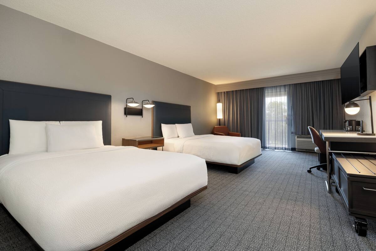 Ein Hotelzimmer mit zwei Betten, einem Schreibtisch und einem Stuhl.