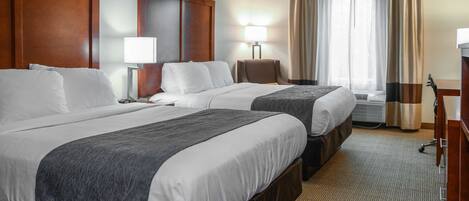 A hotel room with two beds, a desk, a chair, a lamp, and a window with curtains.