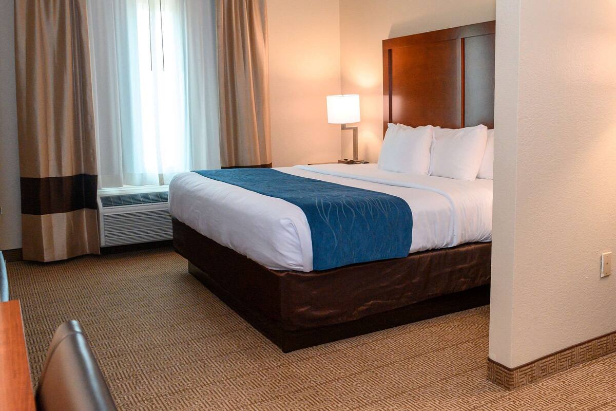 Ett hotellrum med en stor säng, ett skrivbord och ett fönster med gardiner.