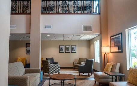A spacious lobby with a high ceiling, a mezzanine level, and multiple seating areas including sofas and chairs.