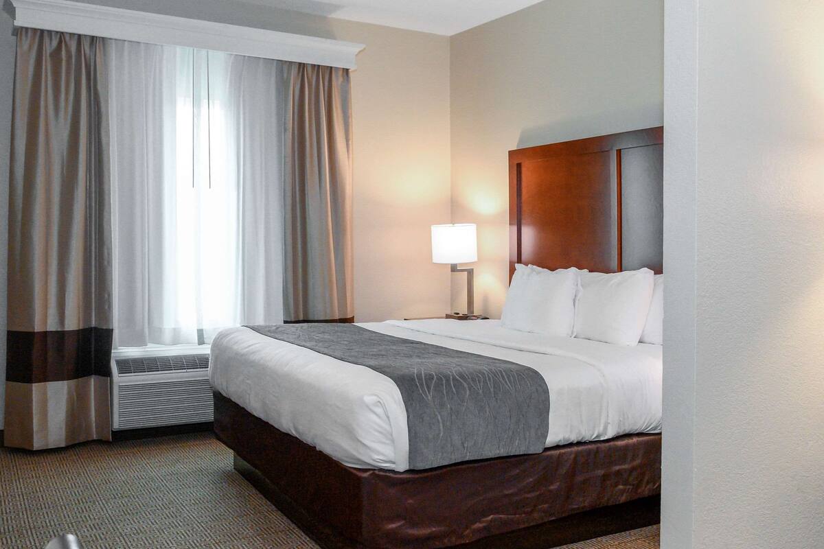 Ett hotellrum med en stor säng, en sänglampa och ett fönster med gardiner.