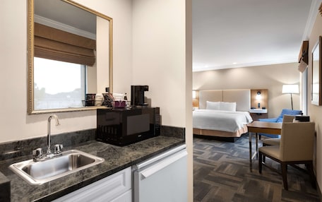 A hotel room with a kitchen area, including a sink, microwave, and a dining table with chairs.