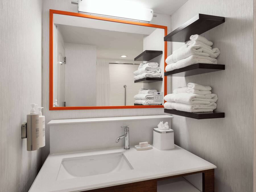 Un baño moderno con un lavamanos blanco, un espejo con marco naranja y repisas con toallas dobladas.