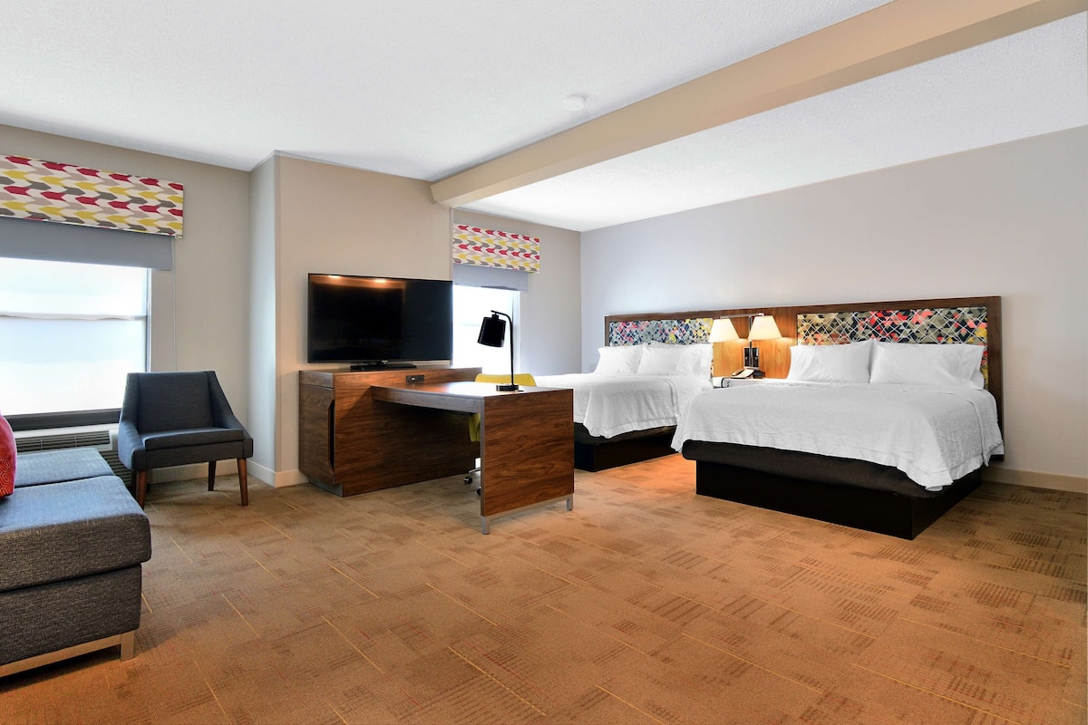 A hotel room with a bed, a desk with a TV, a chair, and a couch.