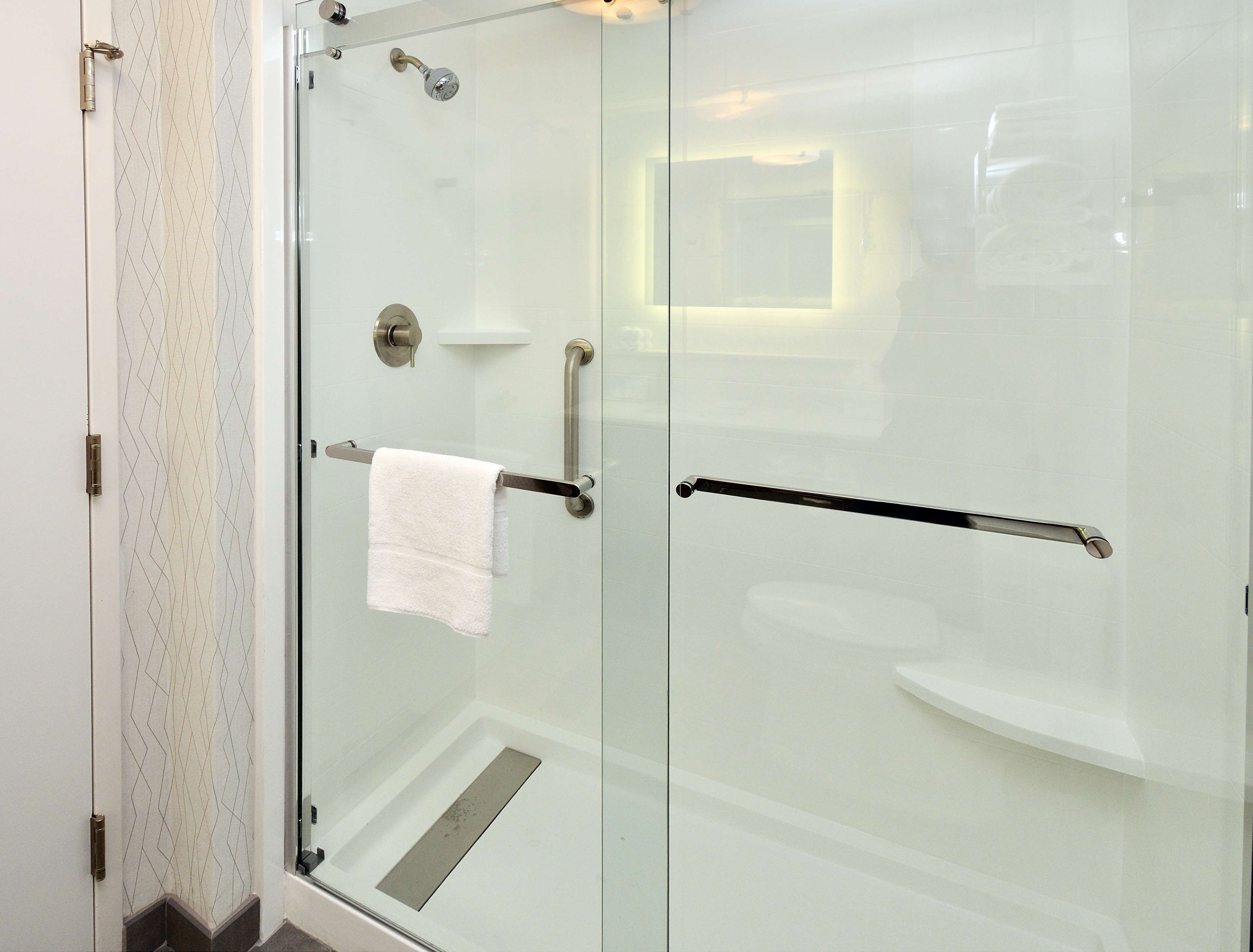 A modern bathroom with a glass shower enclosure, a towel rack, and a handrail.