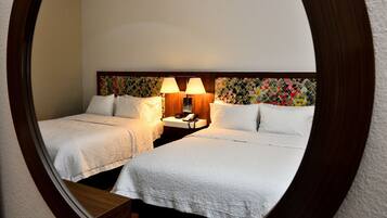 A hotel room with two beds, a nightstand with a lamp, and a patterned headboard.