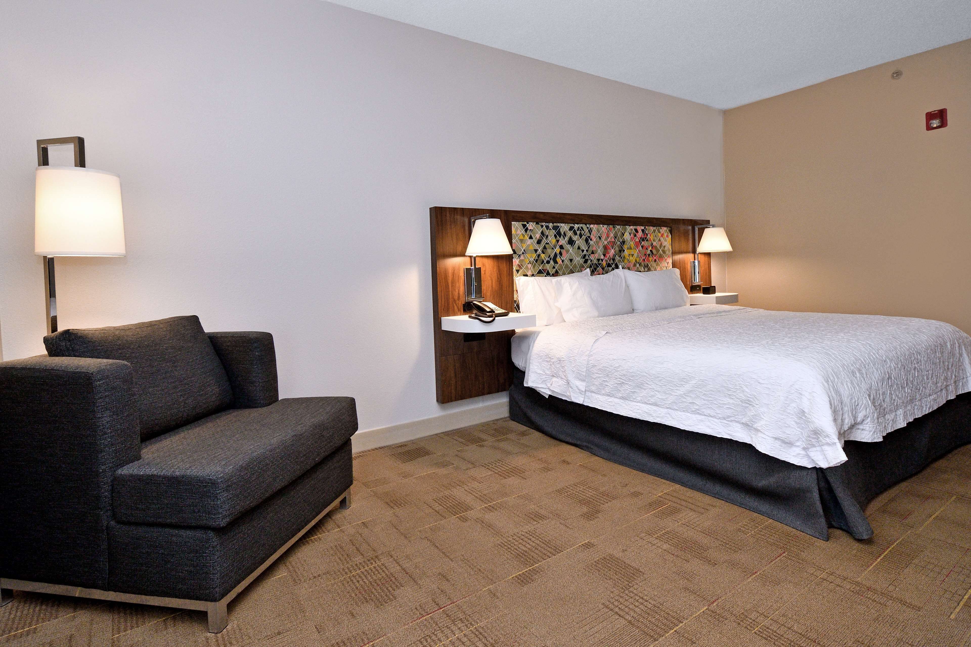 A hotel room with a bed, a sofa, two bedside lamps, and a patterned headboard.