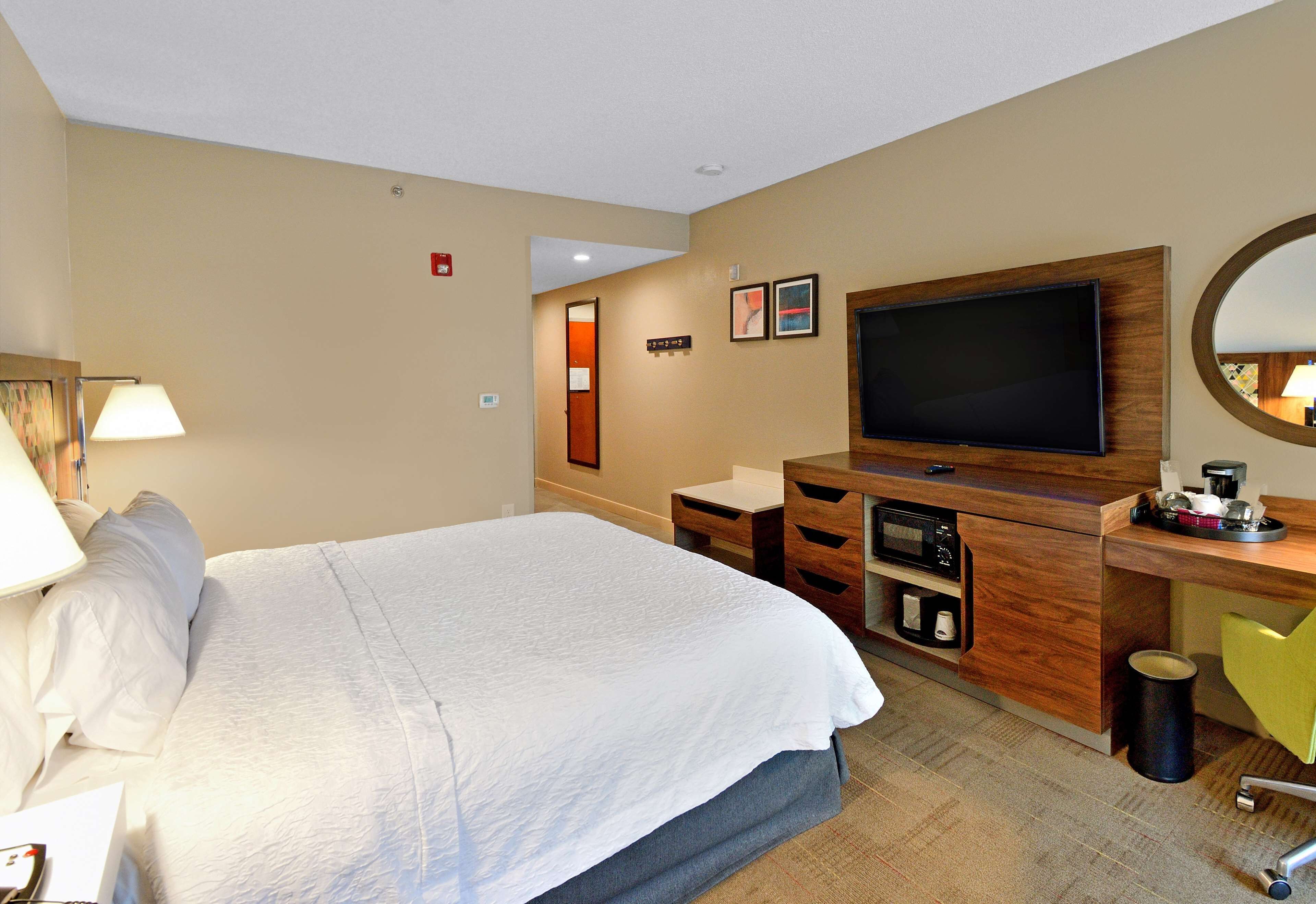 A hotel room with a large bed, a TV, a desk with drawers, a mirror, and a trash can.