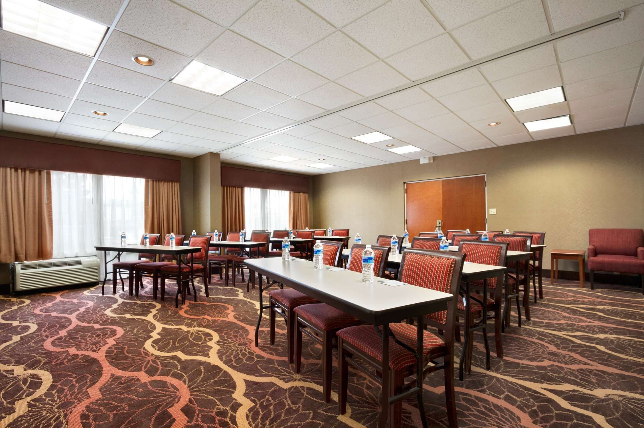 A conference room with multiple tables and chairs, air conditioning, and a carpeted floor.