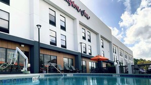 Un hotel moderno con piscina, mobiliario exterior y un cartel que dice "Hampton Inn".