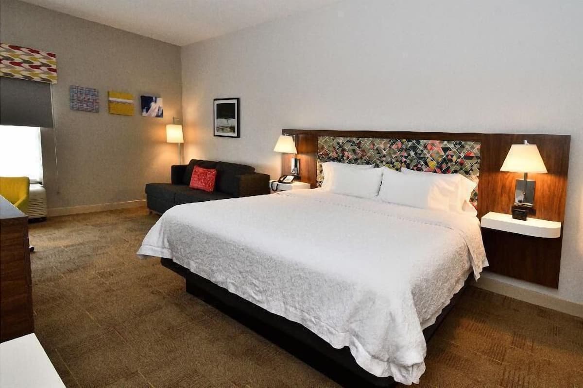 A hotel room with a large bed, two bedside tables with lamps, a sofa, and a small table with a lamp.