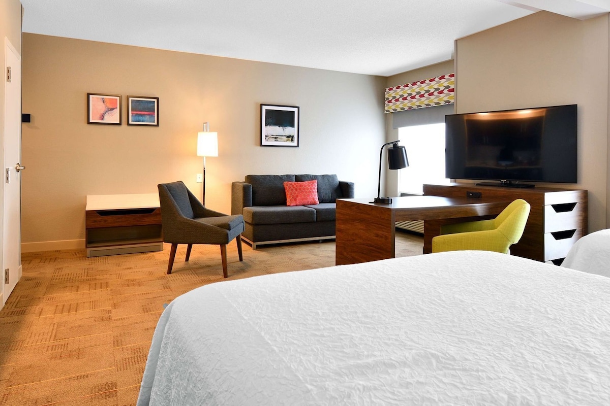 Una habitación de hotel con cama, sofá, escritorio, televisor y lámpara.