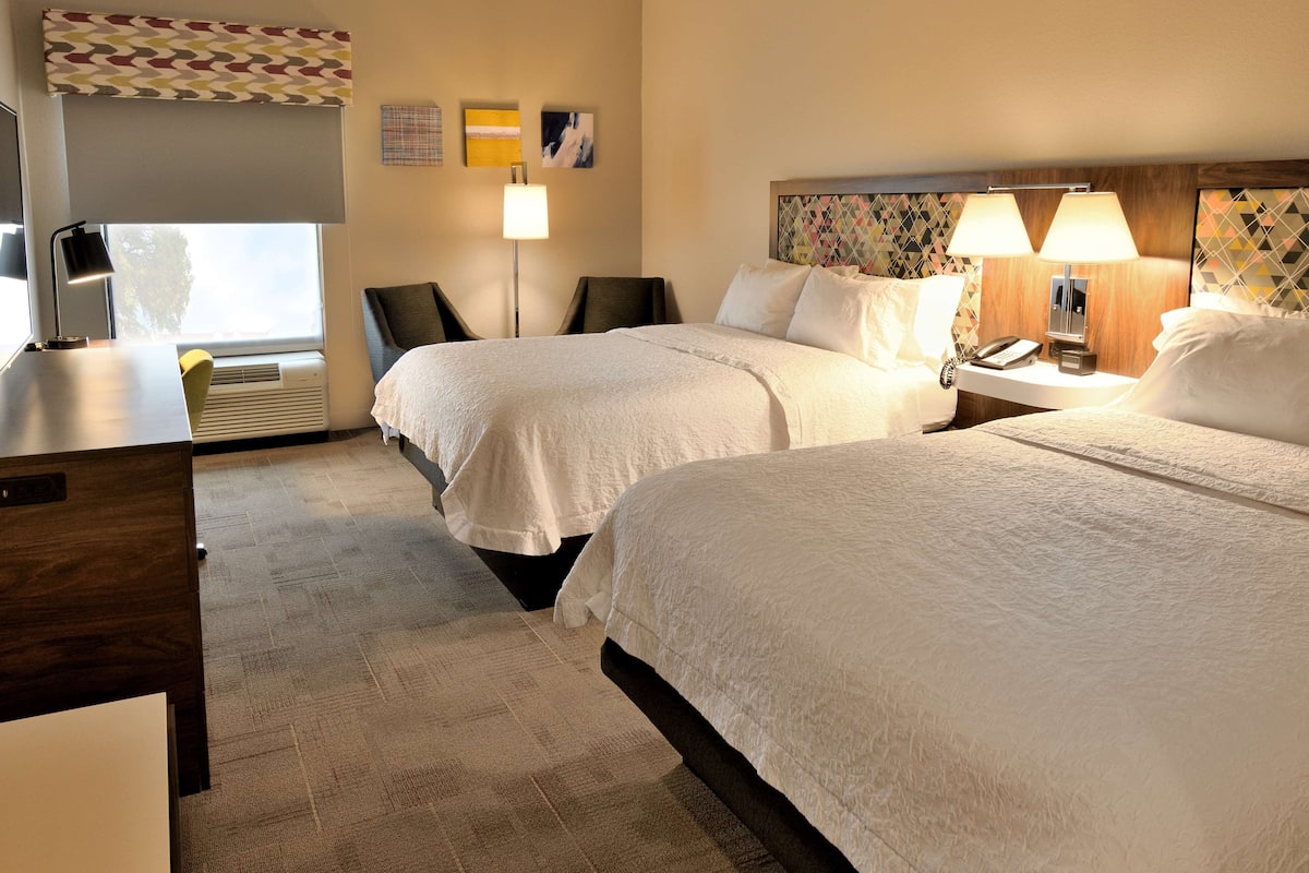 A hotel room with two beds, a desk, a chair, a lamp, and a phone on the nightstand.