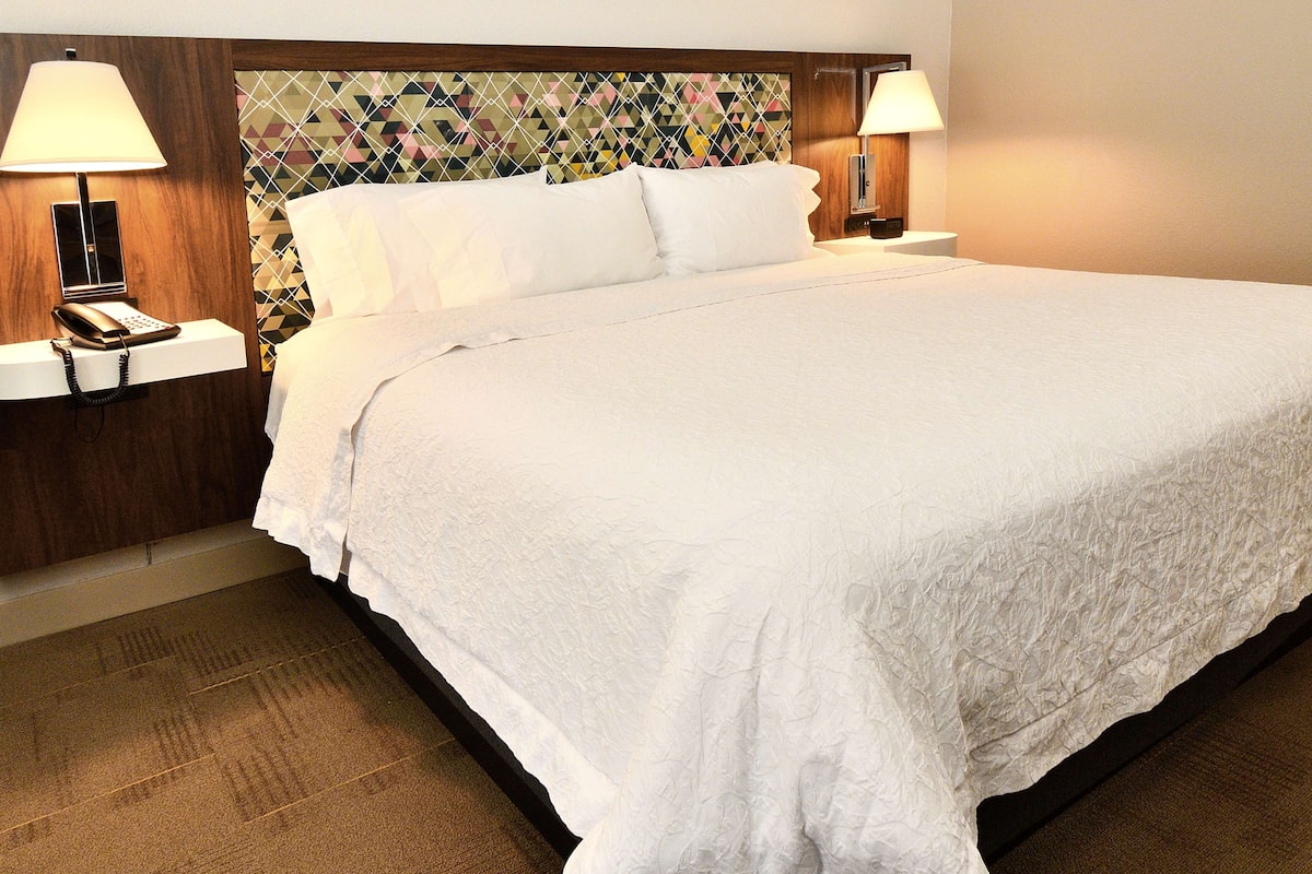 A neatly made bed with white linens, a patterned headboard, and bedside lamps on either side.