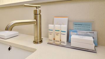 Uma bancada de banheiro com pia, torneira e produtos de higiene pessoal, incluindo shampoo, condicionador e loção corporal.