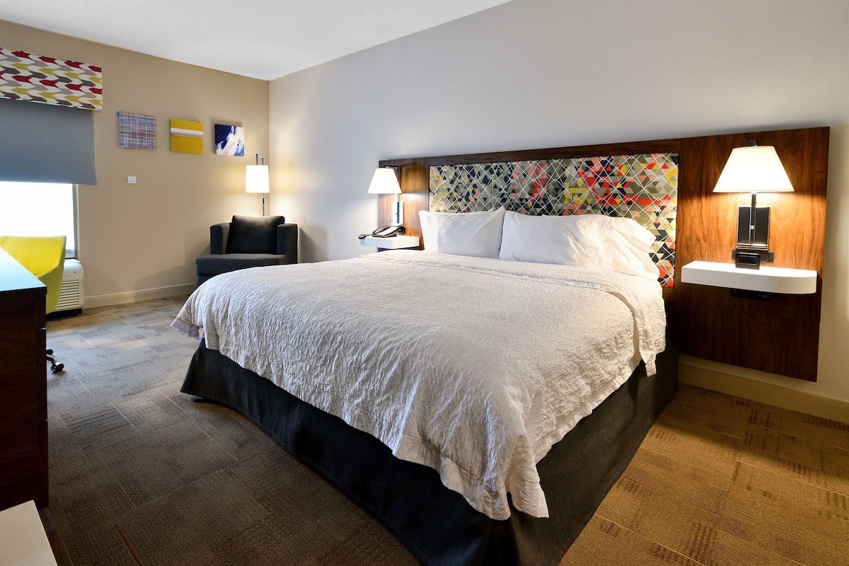 A hotel room with a large bed, two bedside tables with lamps, a chair, and a desk.