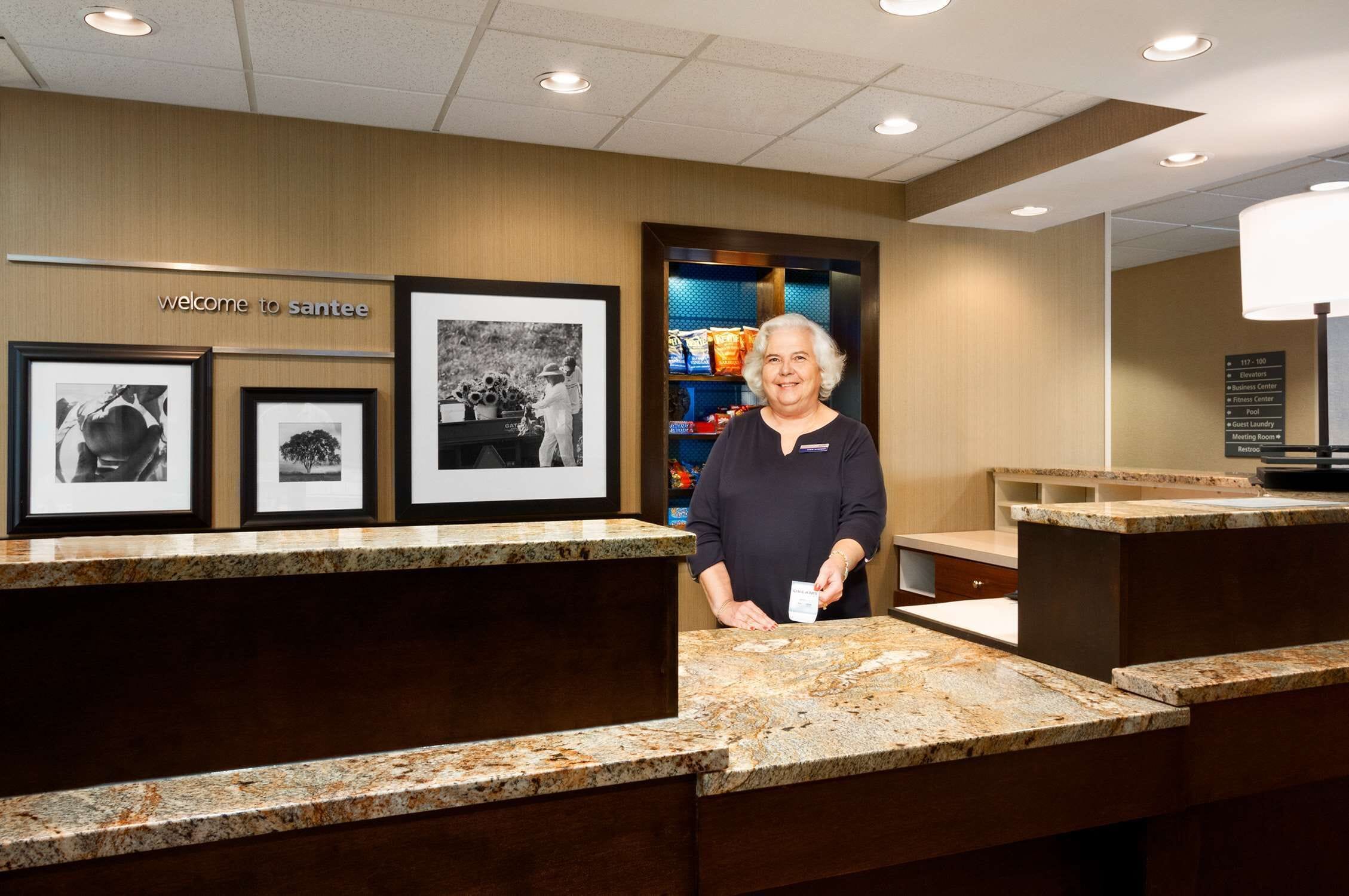 A reception area with a 'Welcome to Santee' sign, framed black and white photographs, and a counter with a name tag holder.