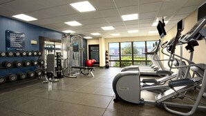 Un gimnasio con cintas de correr, máquinas de pesas y una pared de mancuernas.