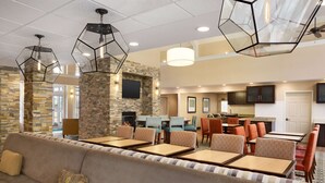 Un hall de hotel con una zona de estar, una chimenea, un televisor montado en una pared de piedra y una cocina al fondo.