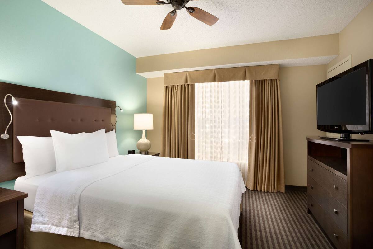 Ein Hotelzimmer mit einem großen Bett, einem Fernseher, einem Nachttisch und einem Deckenventilator.