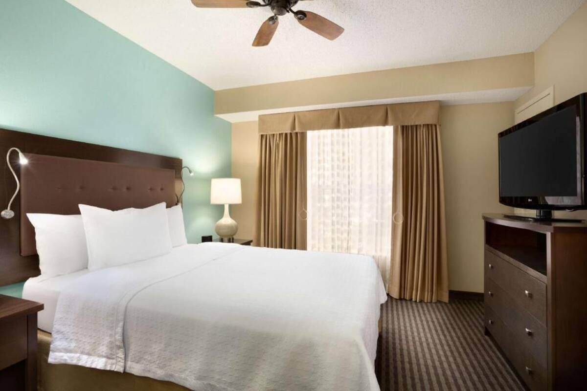 Ein Hotelzimmer mit Bett, Fernseher, Nachttisch, Lampe und Deckenventilator.