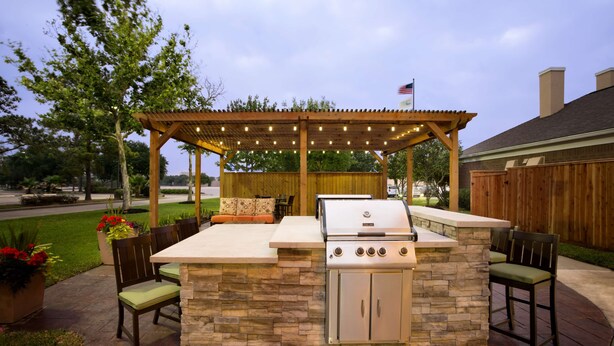 Un patio al aire libre con una estación de barbacoa de piedra, asientos y una pérgola con luces.