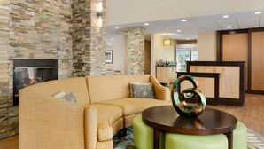 Un moderno hall de entrada con pared de piedra, chimenea, sofá curvo y una mesa redonda con un jarrón decorativo.