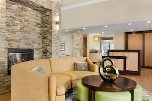 Un moderno hall de entrada con pared de piedra, chimenea, sofá curvo y una mesa redonda con un jarrón decorativo.