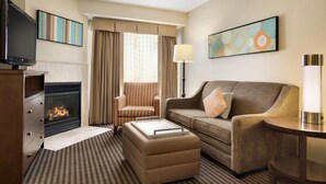 Habitación de hotel con chimenea, sofá, sillón, televisión y obras de arte en las paredes.