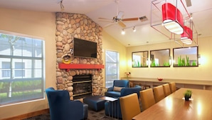 Una sala de conferencias con pared de piedra, un televisor de pantalla plana, chimenea, sillas azules, mesa de madera y ventilador de techo.
